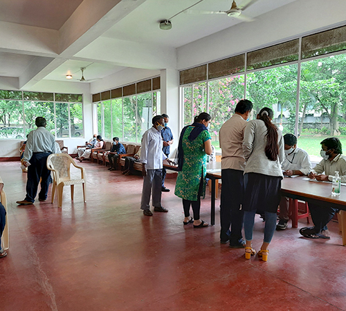 person writing in a notebook beside by an iPad, laptop, printed photos, spectacles, and a cup of coffee on a saucer